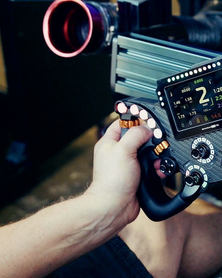 Close-up of a driver’s hands on a professional racing wheel with live lap data on the dash