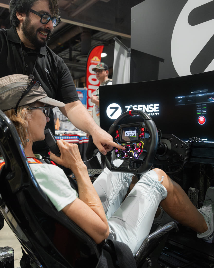 A Trackside crew member coaching a smiling guest at the wheel